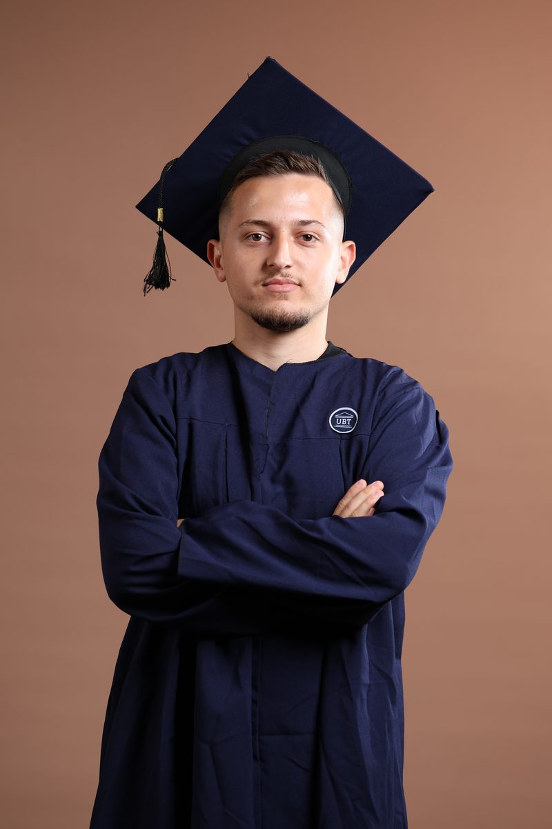 Florent Latifi in a navy UBT graduation gown and cap, arms crossed
